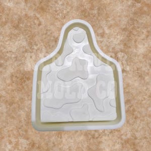May include: A white, rectangular mold with a rounded top, featuring a cowhide pattern. The mold is designed for crafting and has a raised border. The background is a mottled tan color.