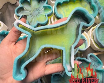 May include: A selection of colourful resin moulds in various shapes, including a dog, flower, and cactus. The dog mould is light green with a blue outline. The Red River Mold Co. logo is visible.