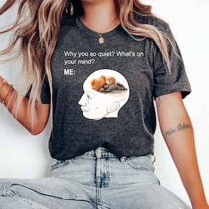 May include: Dark gray t-shirt with the text "Why you so quiet? What's on your mind? ME:". The shirt features a graphic of a head with a brain image of two teddy bears. The person is wearing blue jeans and white shoes.