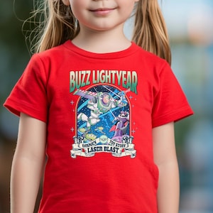 May include: A red t-shirt featuring a graphic of Buzz Lightyear from Toy Story. The graphic includes the text "Buzz Lightyear" and "Disney Toy Story Laser Blast". The shirt is being worn by a person.