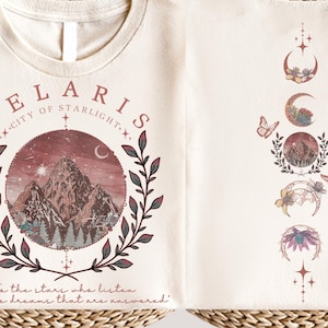 Velaris-themed pink t-shirt with front design of mountains, stars, and 'To the stars who listen' quote. Back highlights moon phases, butterflies, and floral art, blending celestial and fantasy vibes in a stylish, soft fabric.