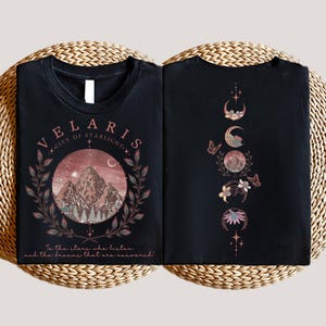Velaris-themed pink t-shirt with front design of mountains, stars, and 'To the stars who listen' quote. Back highlights moon phases, butterflies, and floral art, blending celestial and fantasy vibes in a stylish, soft fabric.
