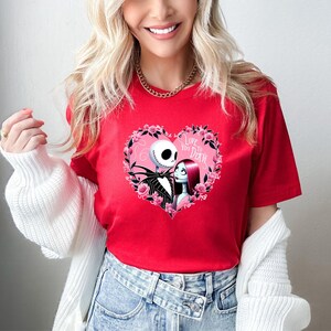 Puede incluir: Camiseta roja con un dise&ntilde;o en forma de coraz&oacute;n con Jack Skellington y Sally de Pesadilla antes de Navidad. El coraz&oacute;n est&aacute; rodeado de rosas rosas y el texto "Love You To Death".