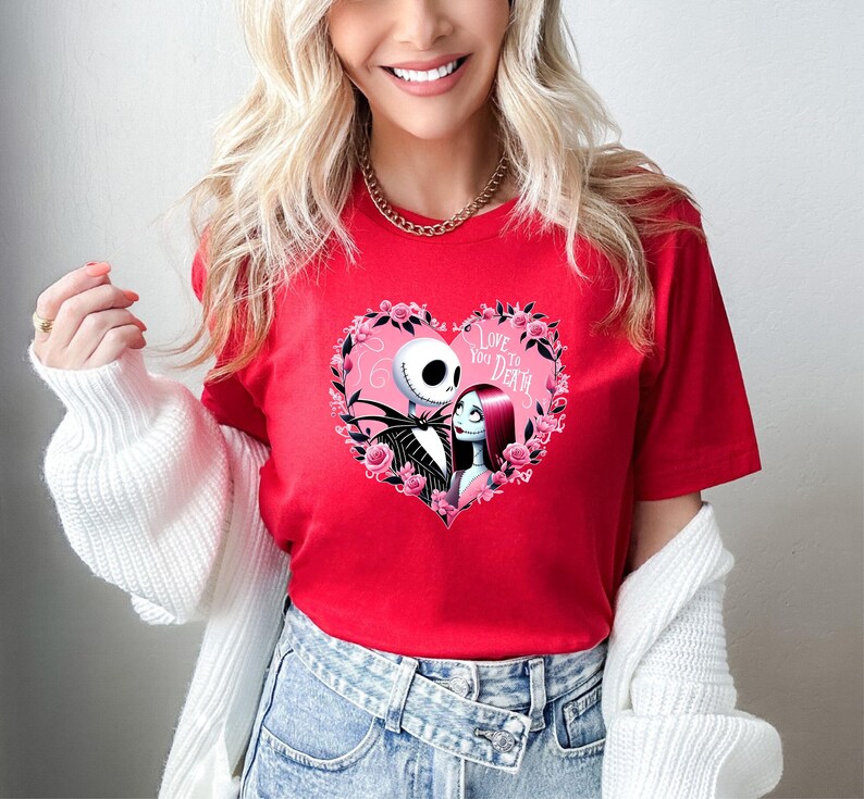 Puede incluir: Camiseta roja con un dise&ntilde;o en forma de coraz&oacute;n con Jack Skellington y Sally de Pesadilla antes de Navidad. El coraz&oacute;n est&aacute; rodeado de rosas rosas y el texto "Love You To Death".