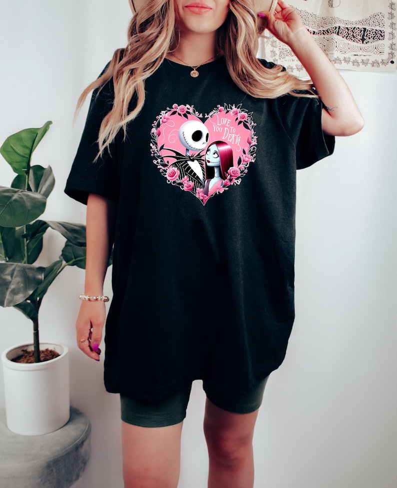 Puede incluir: Camiseta negra con un dise&ntilde;o en forma de coraz&oacute;n que presenta a Jack Skellington y Sally de The Nightmare Before Christmas, rodeados de rosas rosas. El texto "Love You to Death" tambi&eacute;n est&aacute; incluido. Prenda de vestir casual.