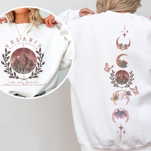Velaris-themed pink t-shirt with front design of mountains, stars, and 'To the stars who listen' quote. Back highlights moon phases, butterflies, and floral art, blending celestial and fantasy vibes in a stylish, soft fabric.
