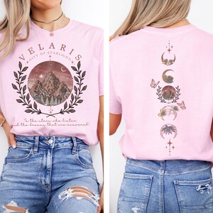 Velaris-themed pink t-shirt with front design of mountains, stars, and 'To the stars who listen' quote. Back highlights moon phases, butterflies, and floral art, blending celestial and fantasy vibes in a stylish, soft fabric.