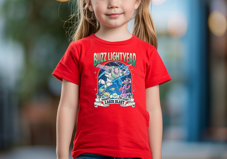 May include: A red t-shirt featuring a graphic of Buzz Lightyear from Toy Story. The graphic includes the text "Buzz Lightyear" and "Disney Toy Story Laser Blast". The shirt is being worn by a person.