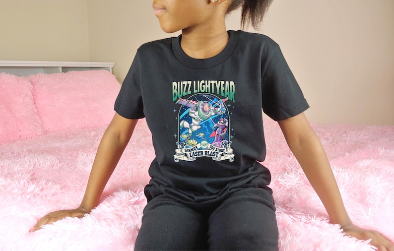 May include: Black t-shirt featuring a graphic of Buzz Lightyear from Toy Story. The design includes the text "Buzz Lightyear" and "Disney Pixar Toy Story Laser Blast". The shirt is worn by a person.