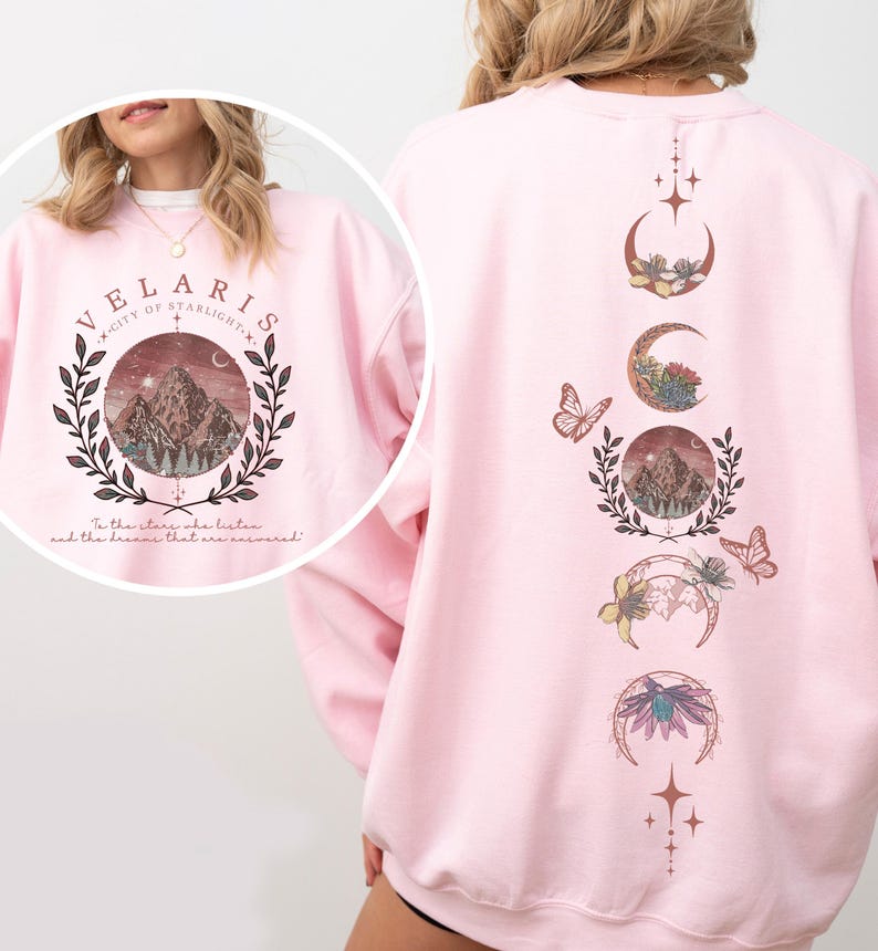 Velaris-themed pink t-shirt with front design of mountains, stars, and 'To the stars who listen' quote. Back highlights moon phases, butterflies, and floral art, blending celestial and fantasy vibes in a stylish, soft fabric.