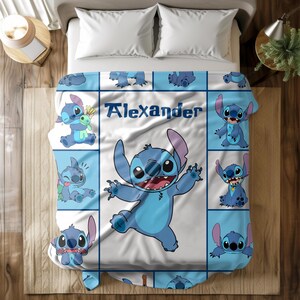 May include: A blue and white blanket featuring the character Stitch from Lilo & Stitch. The blanket has a grid pattern with various Stitch poses and the name "Alexander" in blue text. The blanket is on a bed with white pillows.