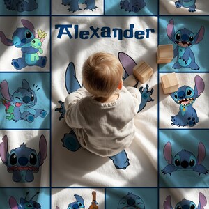 May include: A baby blanket featuring a blue cartoon character design and the name "Alexander" in blue text. The blanket has a white background with blue squares and cartoon character illustrations. Wooden blocks are also present.