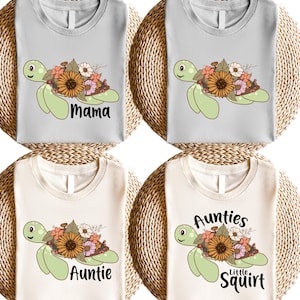 May include: Four t-shirts with a green sea turtle design. The turtles are decorated with flowers and have text on them. The text on the shirts reads "Mama", "Auntie", "Aunties", and "Little Squirt".