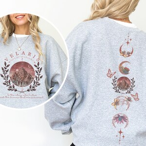 Velaris-themed pink t-shirt with front design of mountains, stars, and 'To the stars who listen' quote. Back highlights moon phases, butterflies, and floral art, blending celestial and fantasy vibes in a stylish, soft fabric.