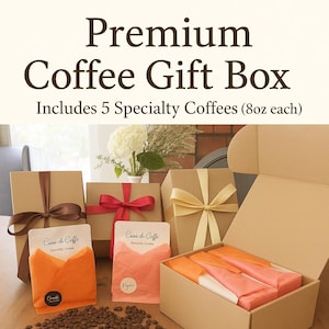 May include: A premium coffee gift box with the text "Premium Coffee Gift Box" and "Includes 5 Specialty Coffees (8oz each)". The box contains five wrapped coffee packages and several gift boxes tied with ribbons. The coffee beans are scattered on the table.