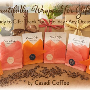K&ouml;nnte beinhalten: Eine Auswahl an Geschenkboxen und Kaffeep&auml;ckchen, gebunden mit B&auml;ndern. Kaffeebohnen sind davor verstreut. Der Text auf dem Bild lautet: "Beautifully Wrapped for Gifting." Bereit zum Verschenken f&uuml;r jeden Anlass.