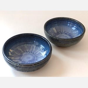 May include: Two blue ceramic bowls with white and blue glaze. The bowls have a slightly rippled texture and a dark blue rim.