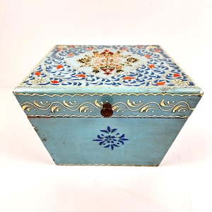 Könnte beinhalten: Eine hellblaue Holzkiste mit einem dekorativen floralen Design, das auf den Deckel gemalt ist. Die Kiste hat einen Messinggriff und ein florales Design auf der Vorderseite.