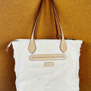 Puede incluir: Bolso tote blanco con estampado de espiga, detalles de cuero marr&oacute;n en las asas y un bolsillo frontal. El bolso tiene cierre de cremallera y un peque&ntilde;o logotipo rectangular.