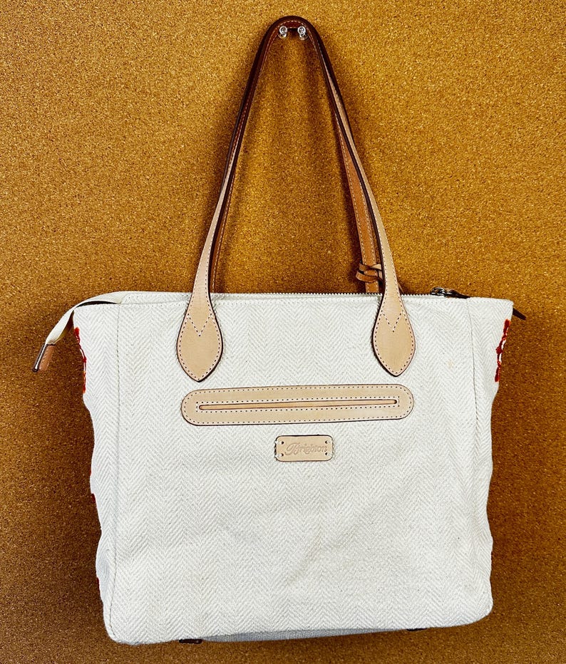 Puede incluir: Bolso tote blanco con estampado de espiga, detalles de cuero marr&oacute;n en las asas y un bolsillo frontal. El bolso tiene cierre de cremallera y un peque&ntilde;o logotipo rectangular.