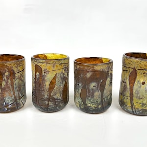 May include: Set of four ceramic drinking glasses with a brown, yellow and blue glaze. The glasses have a unique, abstract design with thin lines and shapes.