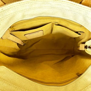 Puede incluir: Vista abierta de un bolso tote beige con un patr&oacute;n de espiga. El interior es de color amarillo claro con m&uacute;ltiples bolsillos y una etiqueta de cuero. El bolso tiene cierre de cremallera y detalles de cuero.