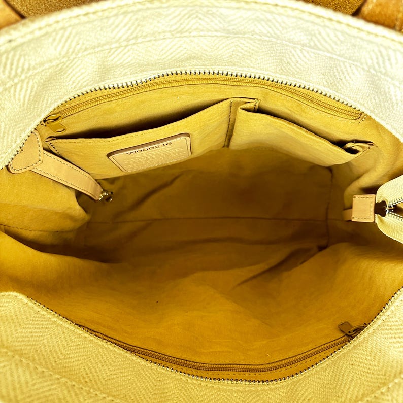 Puede incluir: Vista abierta de un bolso tote beige con un patr&oacute;n de espiga. El interior es de color amarillo claro con m&uacute;ltiples bolsillos y una etiqueta de cuero. El bolso tiene cierre de cremallera y detalles de cuero.