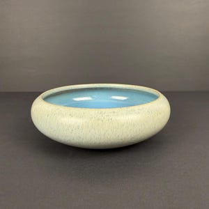 May include: A ceramic bowl with a light green exterior and a bright blue interior. The bowl has a rounded shape and a speckled texture. The bowl is likely used for decorative purposes or for serving food.