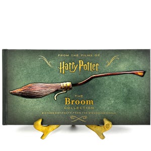 Può includere: Un libro verde con una scritta dorata che recita "From the Films of Harry Potter The Broom Collection Other Artifacts from the Wizarding World". Sulla copertina è raffigurata una scopa marrone e dorata.