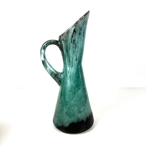 May include: A green ceramic jug with a black rim and a unique glaze pattern. The jug has a wide base and a narrow neck.