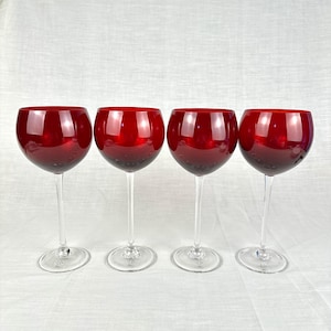Könnte beinhalten: Vier Rotweingläser mit klaren Stielen und Böden. Die Kelche der Gläser sind tiefrot. Die Gläser sind gleichmäßig verteilt und stehen auf einer weißen Oberfläche.