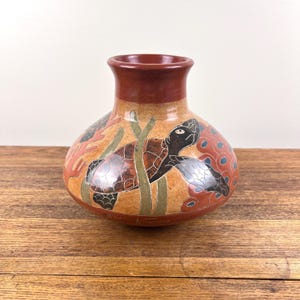 May include: A hand-painted ceramic vase with a brown, orange and green glaze. The vase features a sea turtle swimming through coral and seaweed. The vase is signed "Nicaragua".