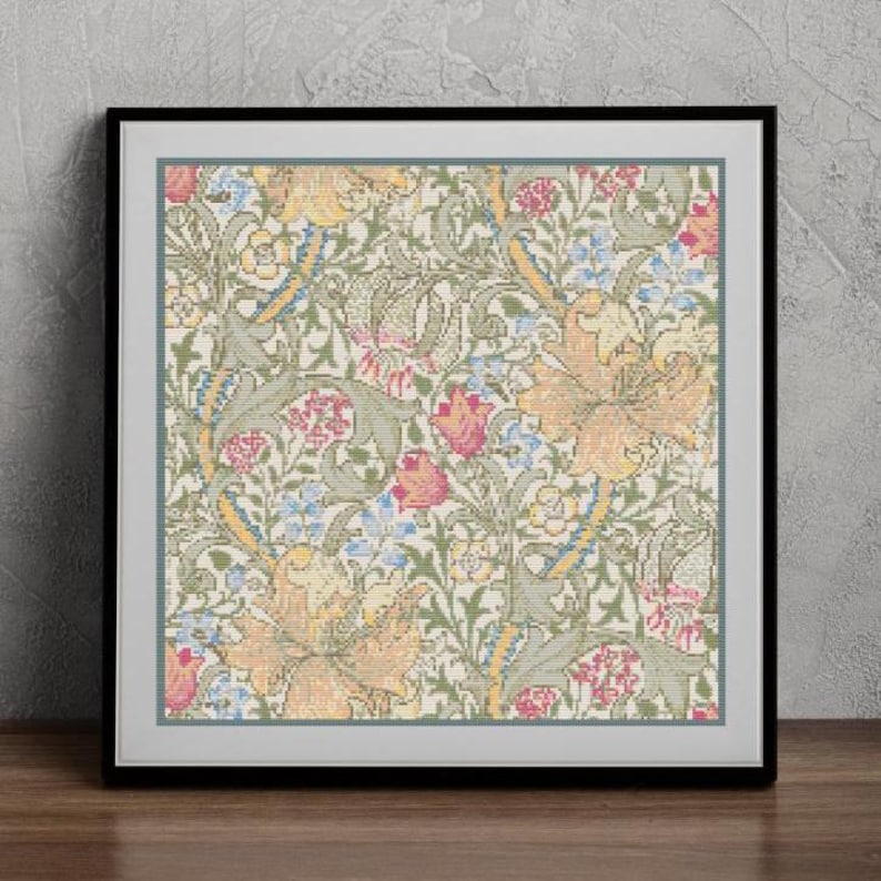 Op de afbeelding: Een ingelijst kruissteekpatroon met een bloemenontwerp met gele, groene, roze en blauwe bloemen. Het patroon is op een witte achtergrond.