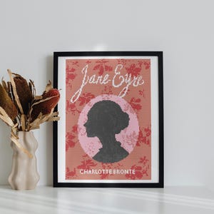 Puede incluir: Una impresión enmarcada de la portada del libro Jane Eyre de Charlotte Brontë. La portada presenta un patrón floral rosa y rojo con una silueta de cabeza de mujer en un círculo rosa.