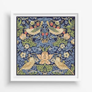 Op de afbeelding: Een ingelijst kruissteekontwerp met een blauwe achtergrond met twee vogels, bloemen en bladeren in tinten groen, geel en rood.