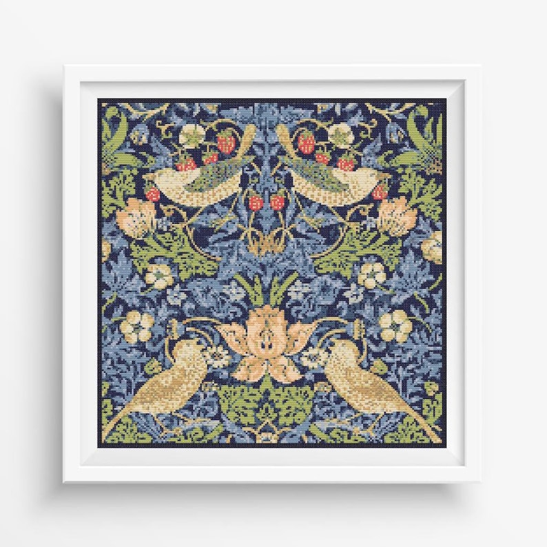 Op de afbeelding: Een ingelijst kruissteekontwerp met een blauwe achtergrond met twee vogels, bloemen en bladeren in tinten groen, geel en rood.