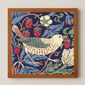 May include: A framed cross-stitch picture showing a bird with a cream body and brown spots, surrounded by red strawberries and green leaves. The background is a dark blue floral pattern, and the frame is wooden.