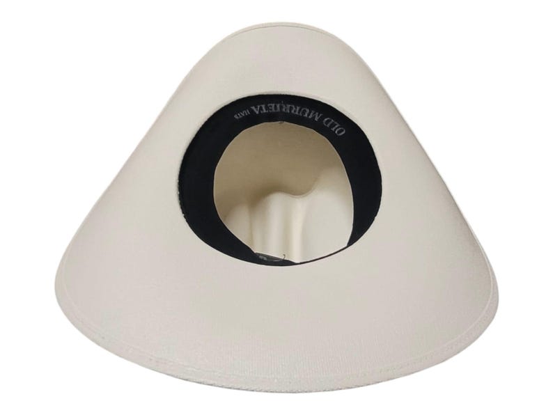 Puede incluir: Sombrero blanco roto con ala ancha y banda interior negra. El interior del sombrero presenta el texto "OLD MURRIETA HATS". El sombrero es de color neutro y tiene un dise&ntilde;o cl&aacute;sico.