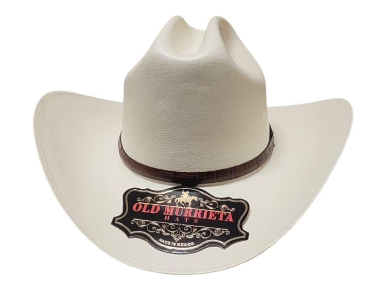Puede incluir: Sombrero de vaquero color crema con una banda de cuero marr&oacute;n. El sombrero tiene un ala ancha y una corona alta. Una etiqueta negra y roja en el ala dice "OLD MURRIETA HATS" y "MADE IN MEXICO".
