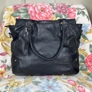 Puede incluir: Bolso tote de cuero negro con asas dobles y una correa para el hombro. El bolso tiene un acabado texturizado, herrajes dorados y un dise&ntilde;o estructurado. Cuenta con m&uacute;ltiples compartimentos y es adecuado para el uso diario.