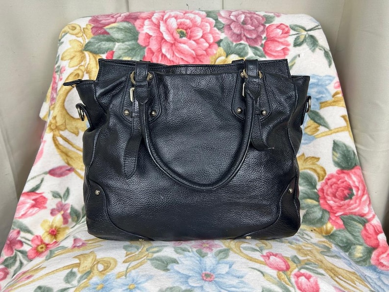 Puede incluir: Bolso tote de cuero negro con asas dobles y una correa para el hombro. El bolso tiene un acabado texturizado, herrajes dorados y un dise&ntilde;o estructurado. Cuenta con m&uacute;ltiples compartimentos y es adecuado para el uso diario.