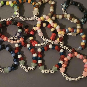 May include: A collection of colourful beaded bracelets with star charms and personalised names, including "LUKA", "KENNING", "BABYBRO", "P3R", "ANORE", "SAD", "ENG", "TOM", "MAJ", "PO3", "CULLY", "IHTH", and "CIA".