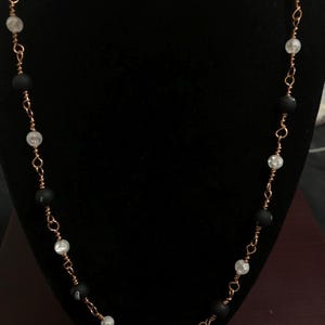 Puede incluir: Un collar con cuentas negras y blancas y una cadena de cobre.