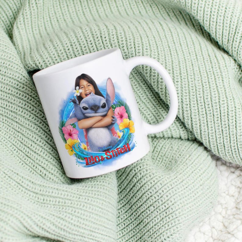 May include: White ceramic mug featuring a colorful graphic of Lilo & Stitch. The design includes Lilo hugging Stitch, surrounded by tropical flowers and the words "Lilo & Stitch" in a stylized font. The mug has a curved handle.