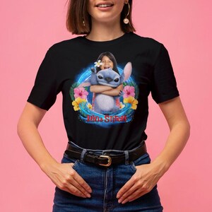May include: Black t-shirt featuring a graphic of Stitch from Lilo & Stitch embracing a person. The design includes a blue and white Stitch, a person with a flower, and the words "Lilo & Stitch" in red and blue.