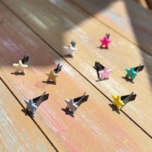 May include: A collection of star-shaped car air fresheners in various colors, including yellow, pink, blue, and white. Each star is attached to a black clip, arranged on a wooden surface.