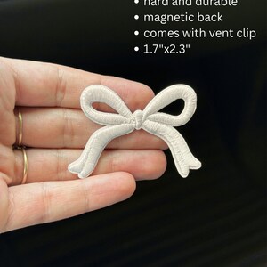 May include: A white embroidered bow patch with a magnetic back and vent clip. The patch is 1.7" x 2.3" and is described as hard and durable.