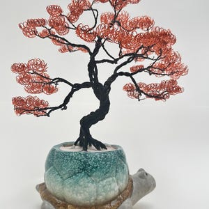 Könnte beinhalten: Handgefertigte Drahtbaumskulptur mit kupferfarbenen Blättern und einem schwarzen Stamm. Der Bonsai-Baum steht in einem türkis-grauen Keramiktopf in Schildkrötenform. Ein einzigartiges Wohnaccessoire.