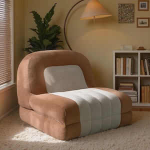 May include: A brown and white inflatable chair is the focal point of a cozy living room. The chair is made of soft, textured material and has a rounded back and armrests. The room features a bookshelf, a window, and a floor lamp.