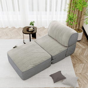 May include: A light gray modular sofa with a matching ottoman. The sofa has a rounded backrest and a quilted pattern on the seat and back. The base and sides are a darker gray. The ottoman is rectangular and has a similar quilted pattern.